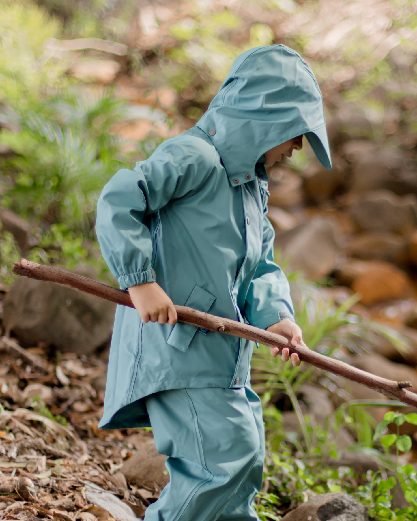 Child in waterproof jacket with mud guard exploring outdoors with a stick, kids rain jacket for messy play