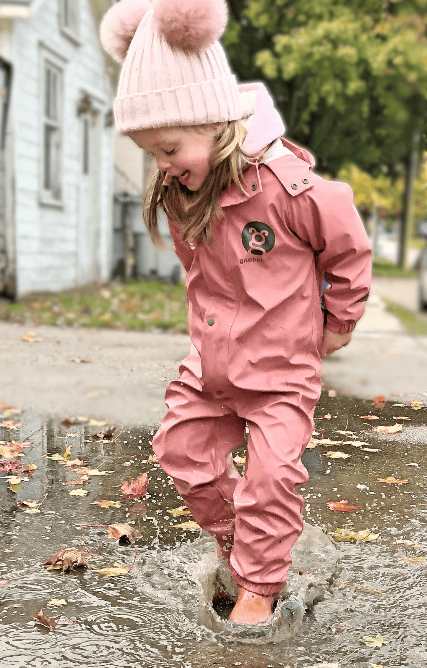 Child in pink waterproof rain suit jumping in puddle, kids rainwear for wet weather outdoor play