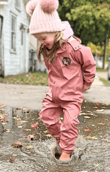 Child in pink waterproof rain suit jumping in puddle, kids rainwear for wet weather outdoor play