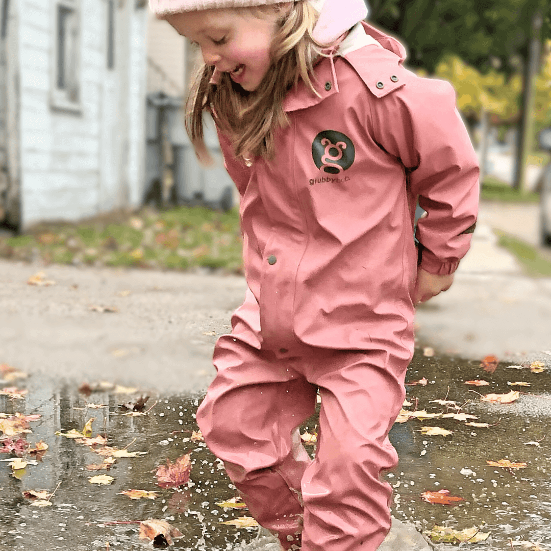Child wearing pink waterproof puddle suit jumping in puddle on footpath