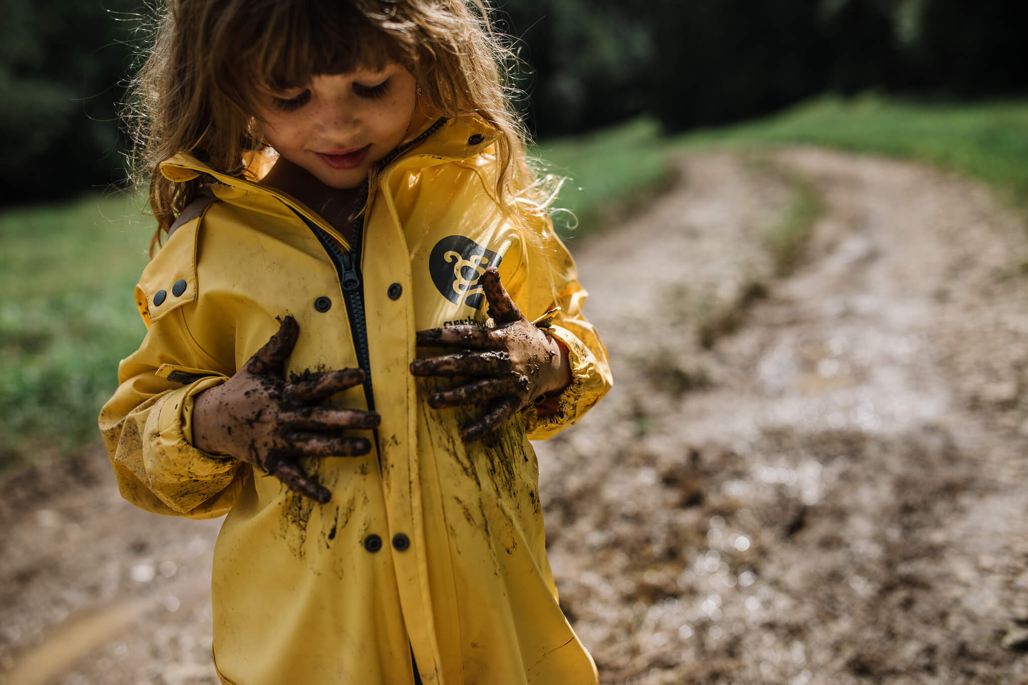 Young girl wearing her nature play waterproof puddle suit and smearing mud over her stomach