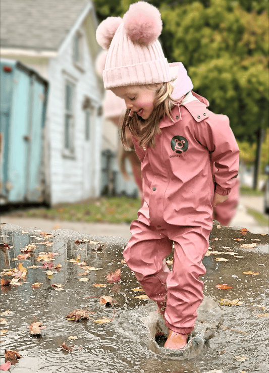 toddler girl in a dusty rose pink waterproof puddle suit splashing in a puddle 