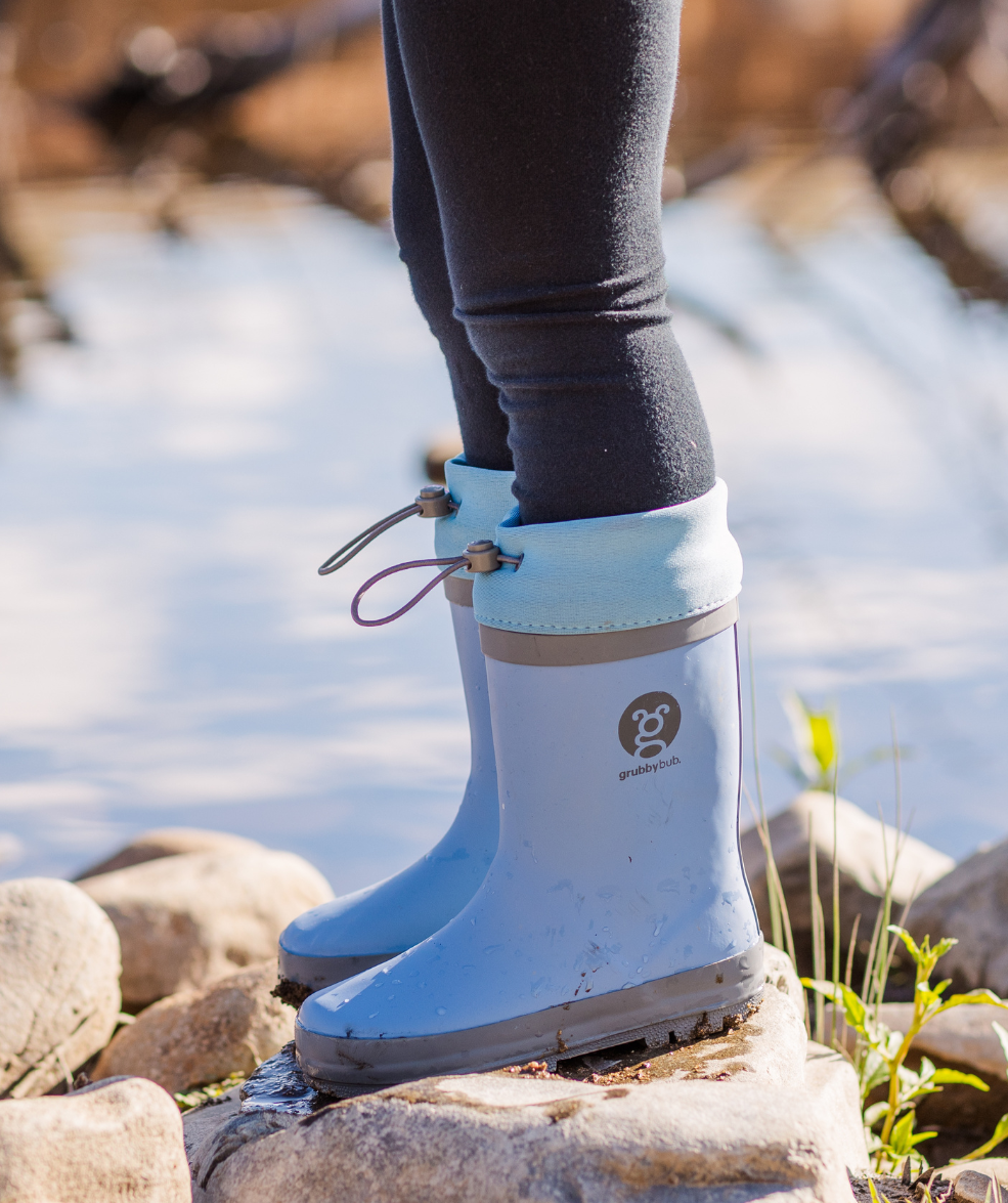 Adjustable toggle top kids gumboots in blue, with child standing on top of a rock