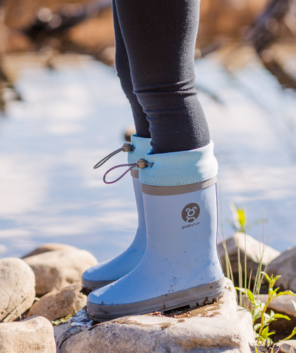 Adjustable toggle top kids gumboots in blue, with child standing on top of a rock