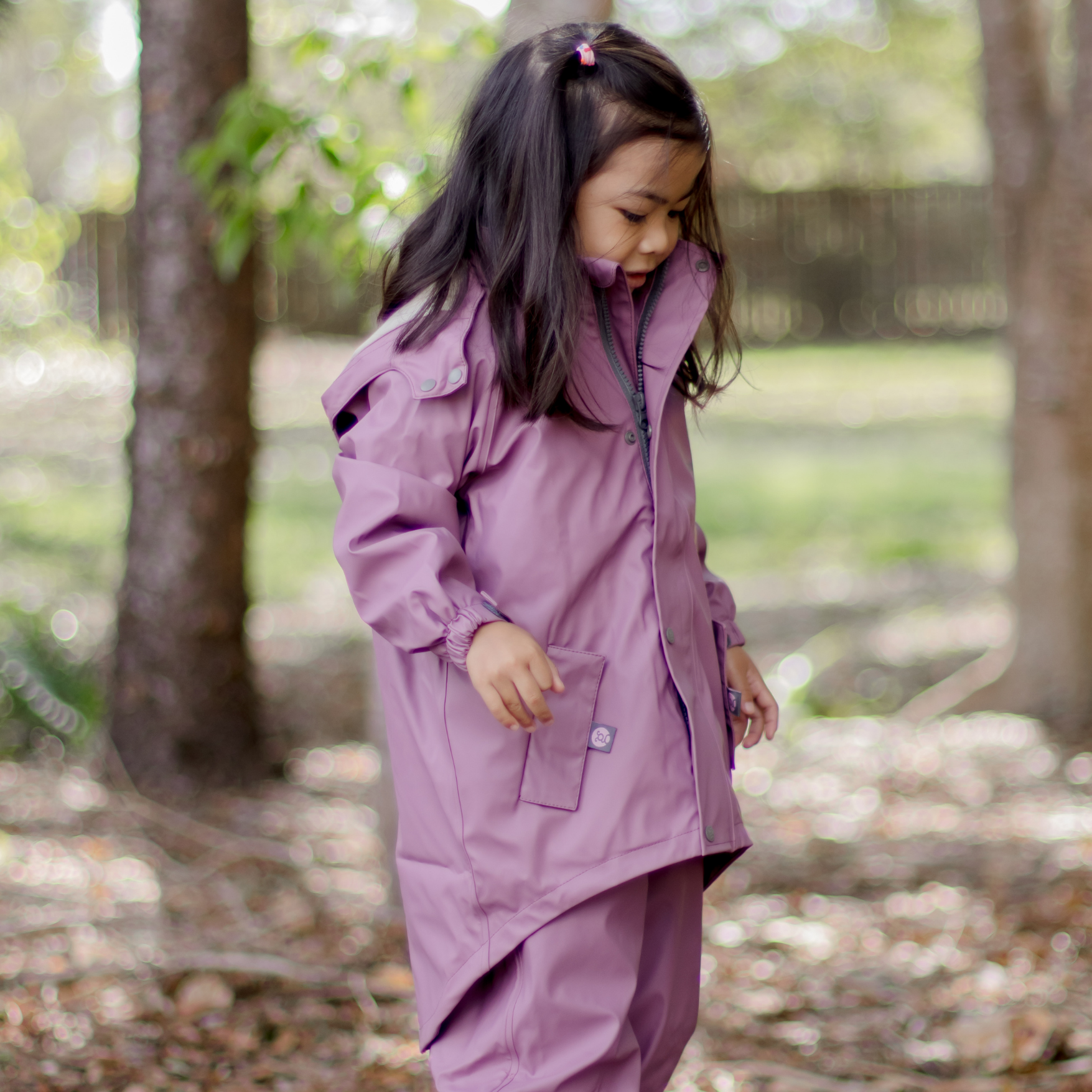 Child wearing a sustainable waterproof purple raincoat with extra long hem in a forest setting