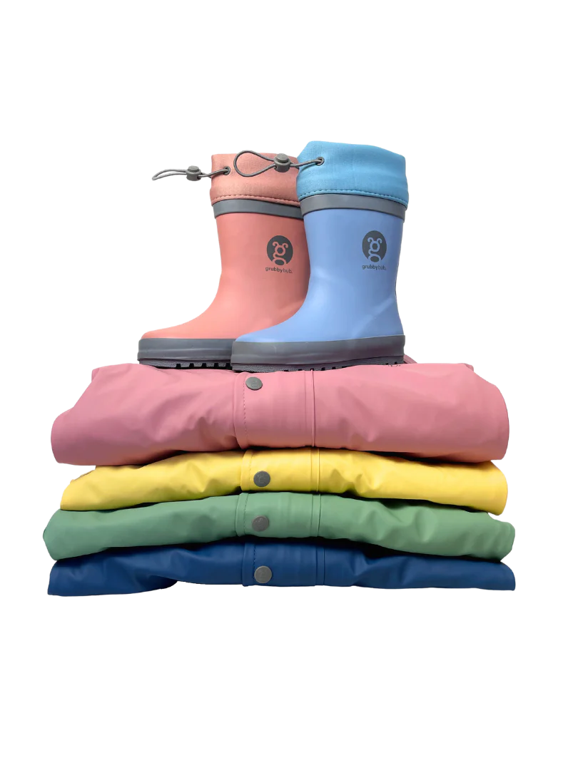 Folded pile of kids rain suits in bright, pastel colours with adjustable toggle top gumboots sitting on top 