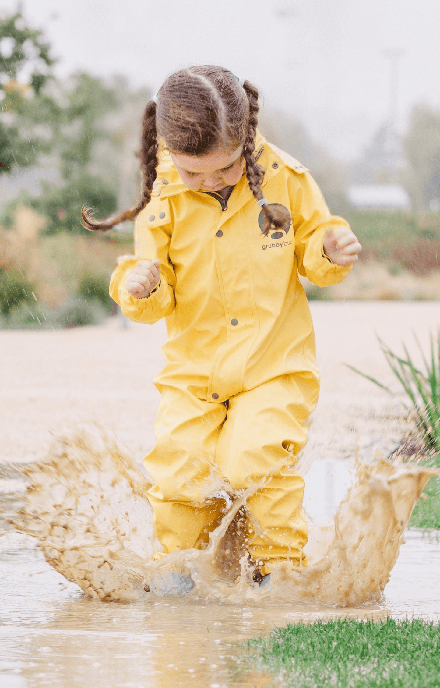 Child in Grubbybub yellow waterproof rain suit jumping in muddy puddle, all weather kids playwear