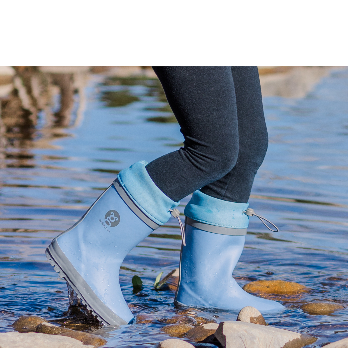 Person wearing blue neoprene topped adjustable rubber boots walking through water with a blurred natural background