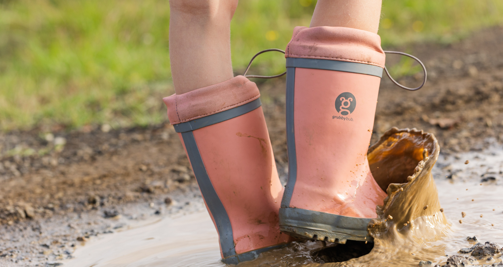A shot of kids legs, wearing just peachy pink gumboots with an adjustable toggle top, splashing in a muddy puddle