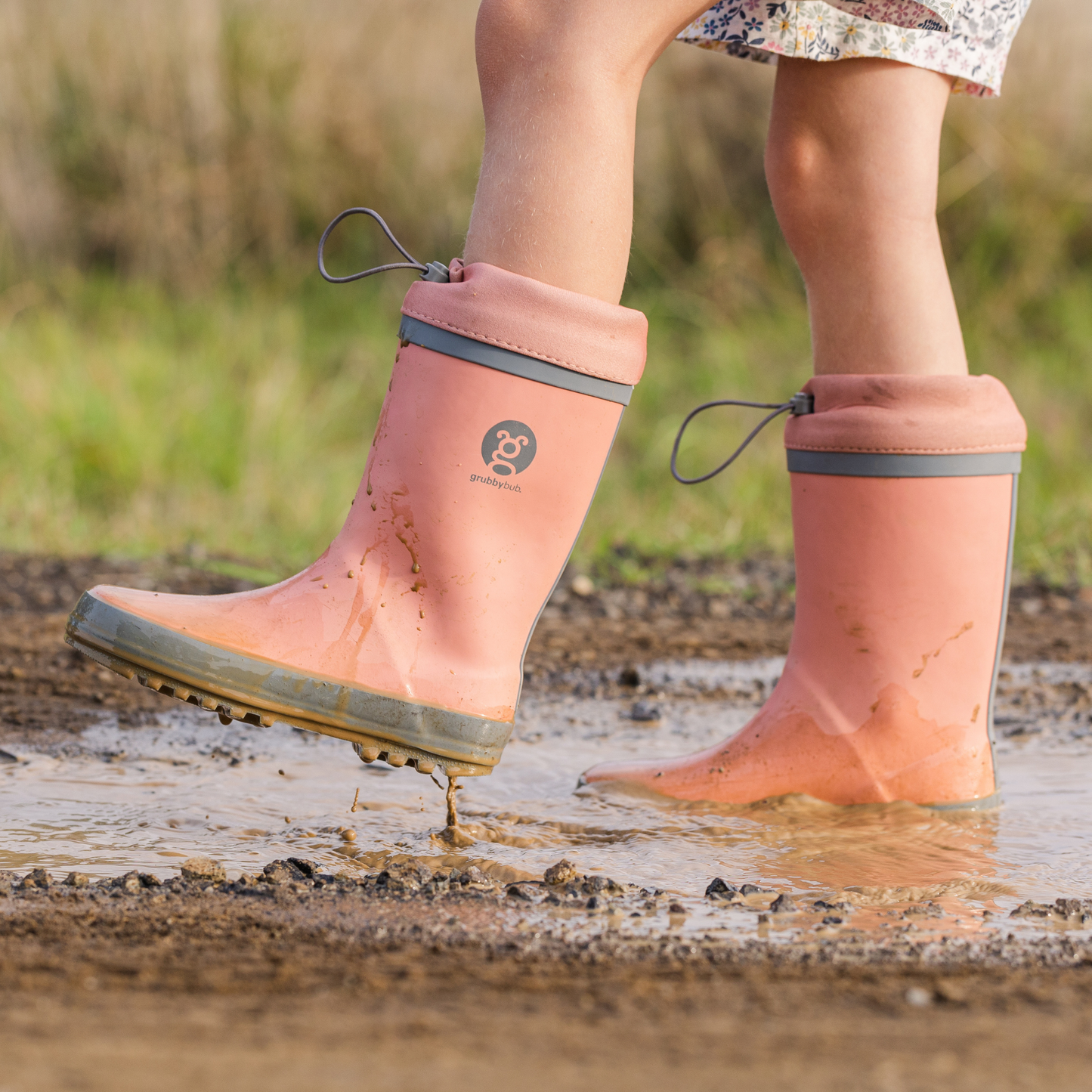 Person wearing neoprene topped adjustable pink rain boots with a visible brand logo, standing in water outdoors.