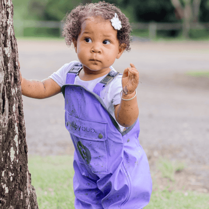 Child in waterproof overalls exploring tree with muddy hands during sensory play